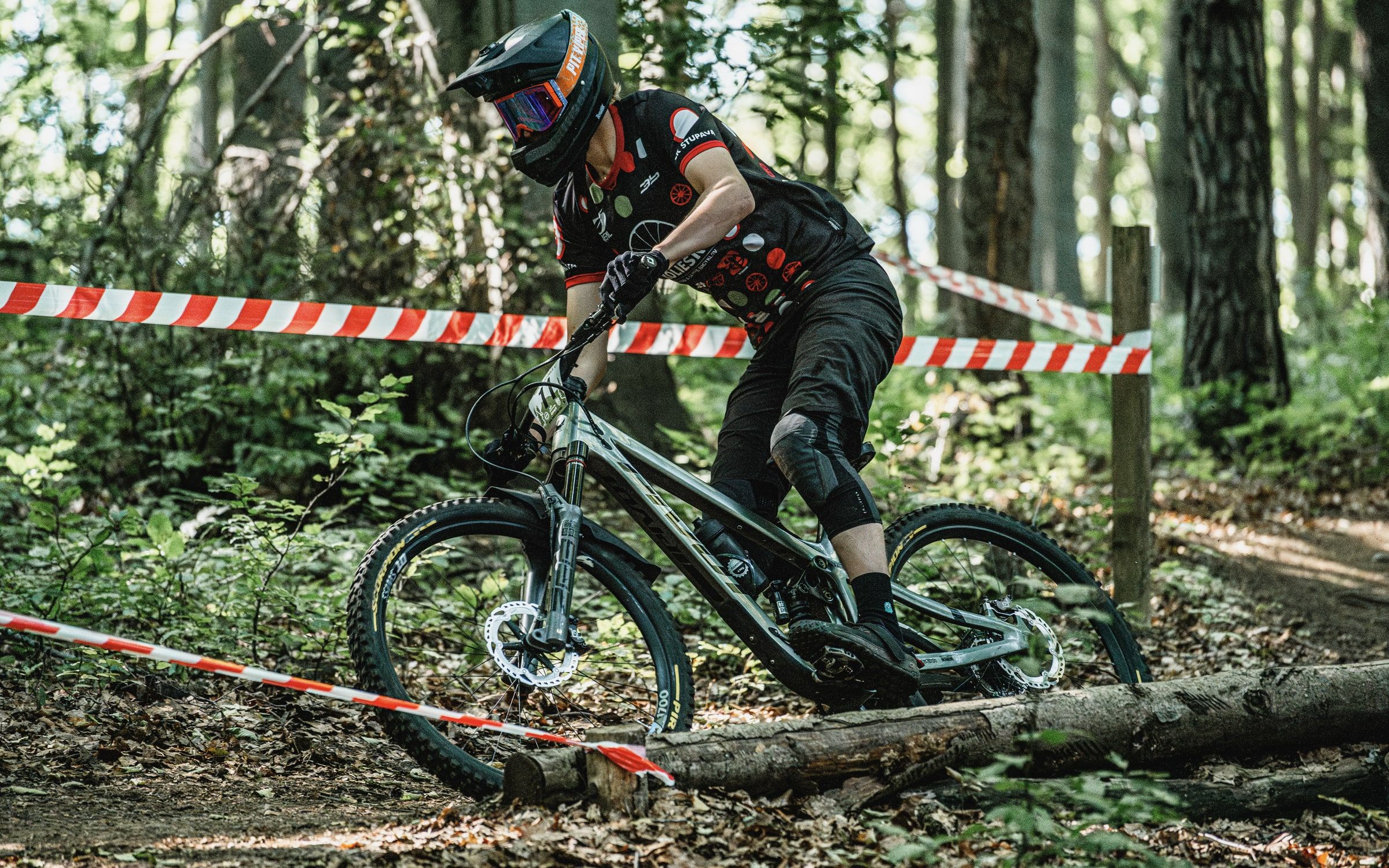 Riding a mountain bike past race tape on a forest enduro track